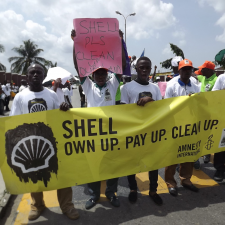 young men holding sign that reads Shell own up. pay up. clean up.